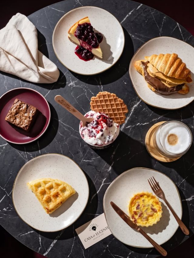 Mesa com cheesecake, croissant, brownie, gelato, cappuccino, waffle e quiche