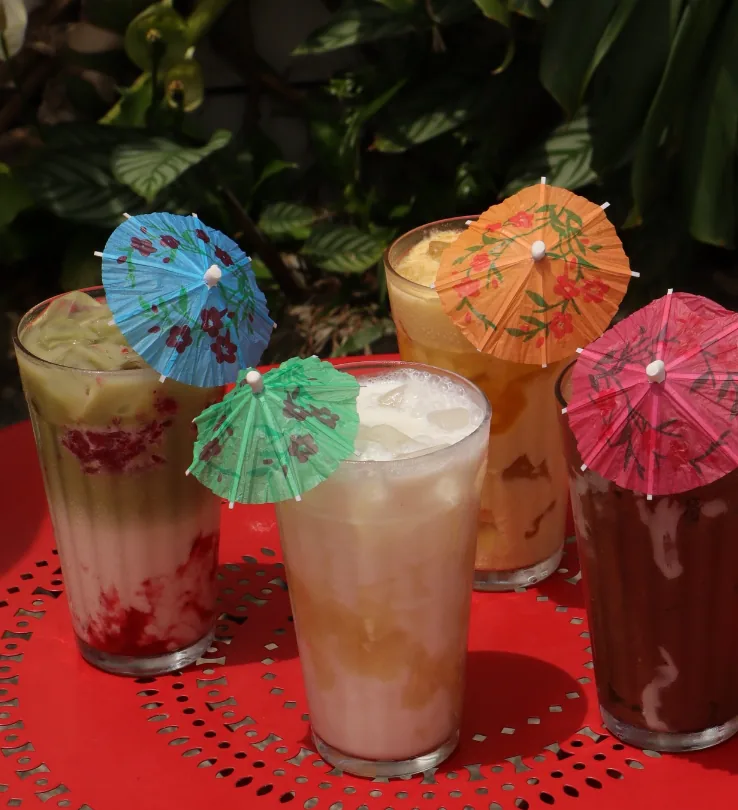Quatro bebidas geladas com guarda-chuvinhas coloridos sobre mesa vermelha