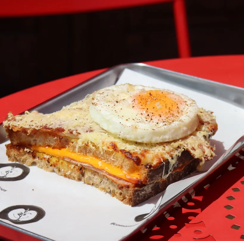 Croque madame com queijo gratinado e ovo por cima, em bandeja de inox
