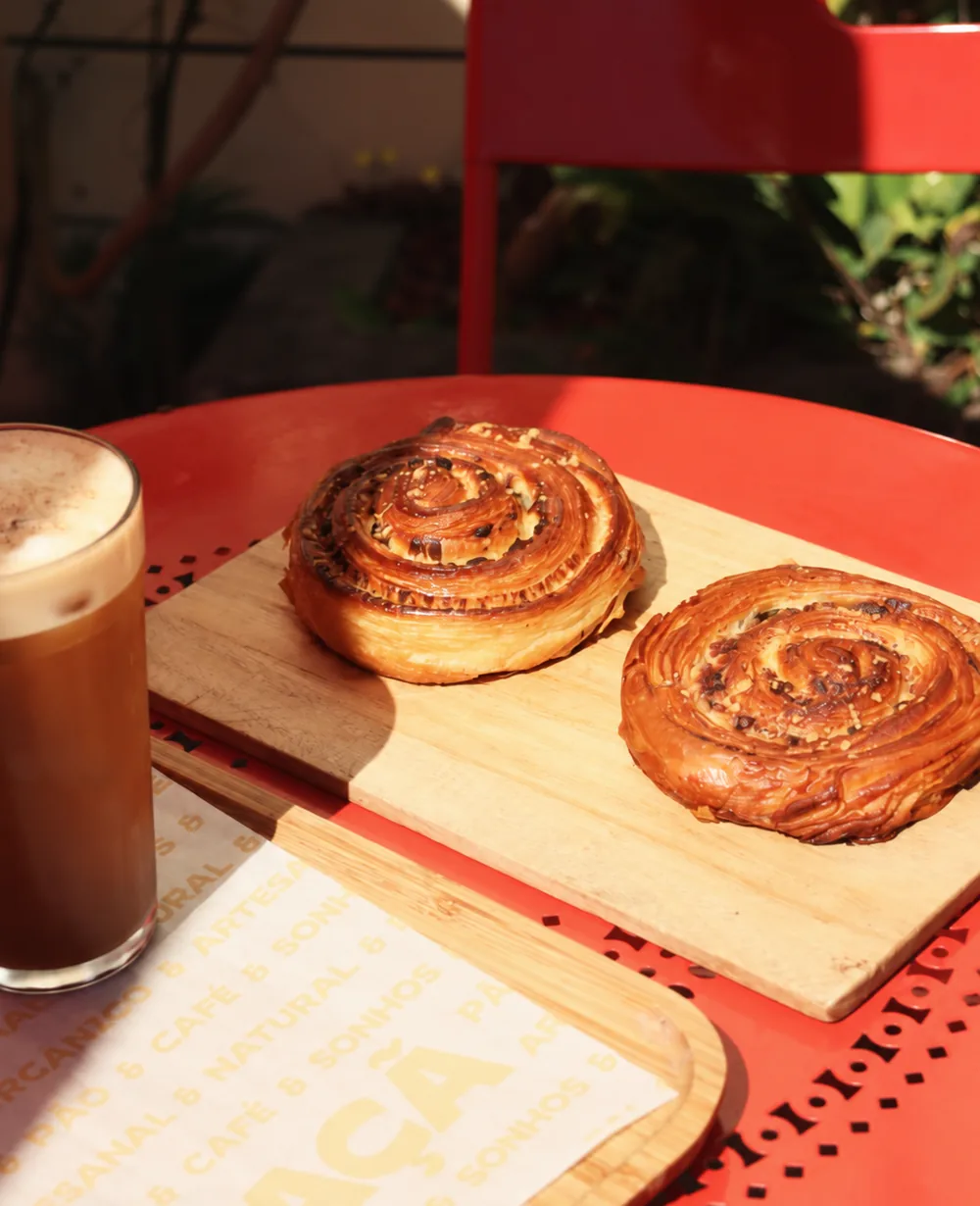 Dois folhados em espiral sobre tábua de madeira ao lado de um café gelado