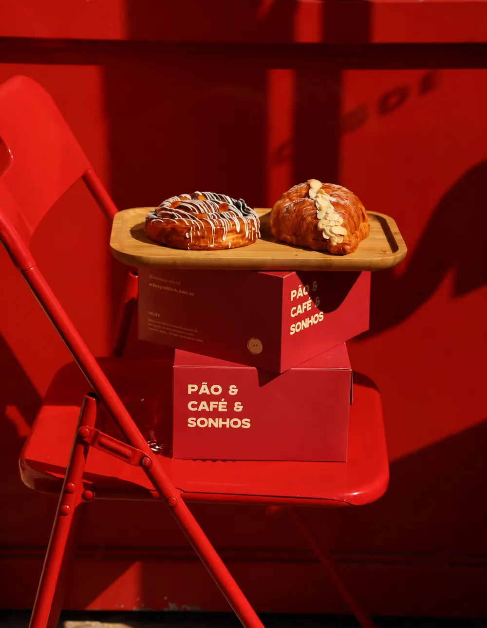 Folhados sobre caixas vermelhas da Maçã escritas Pão & Café & Sonhos, em uma cadeira vermelha