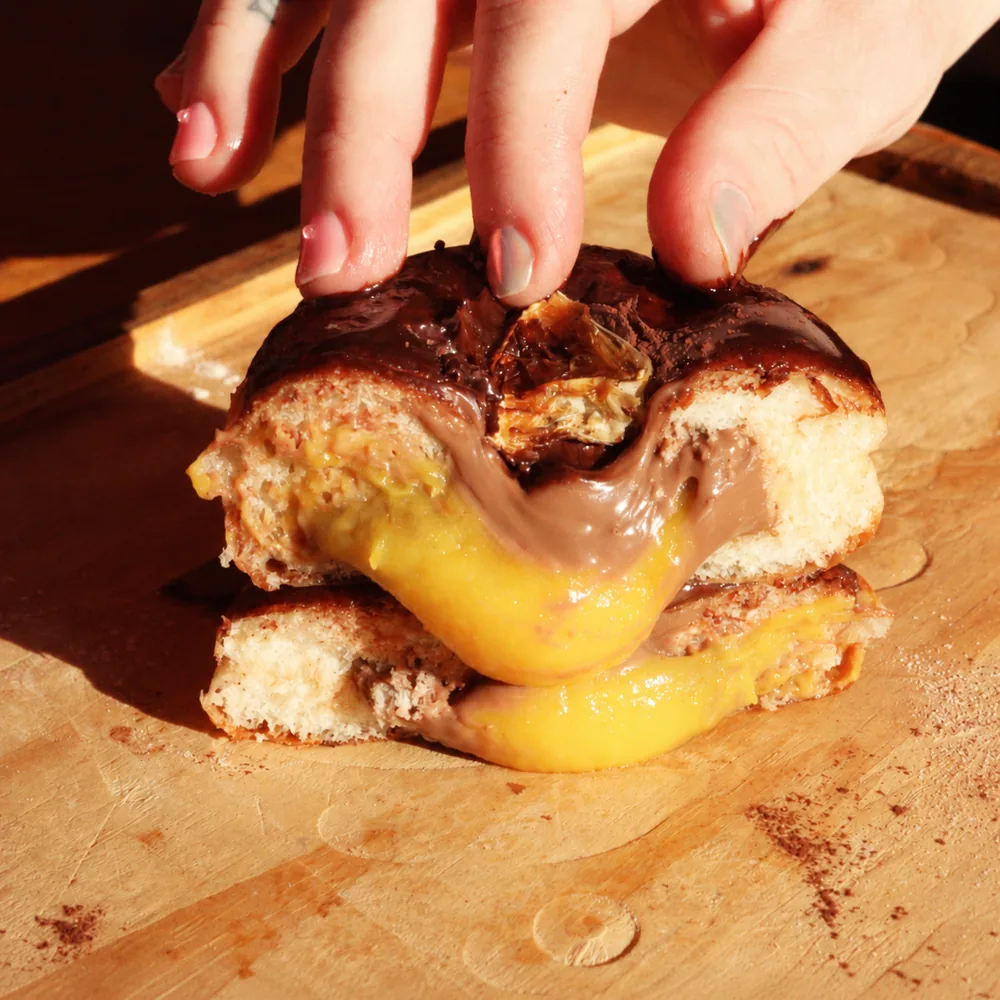Sonho com cobertura de chocolate aberto com as mãos, recheios amarelo e de chocolate