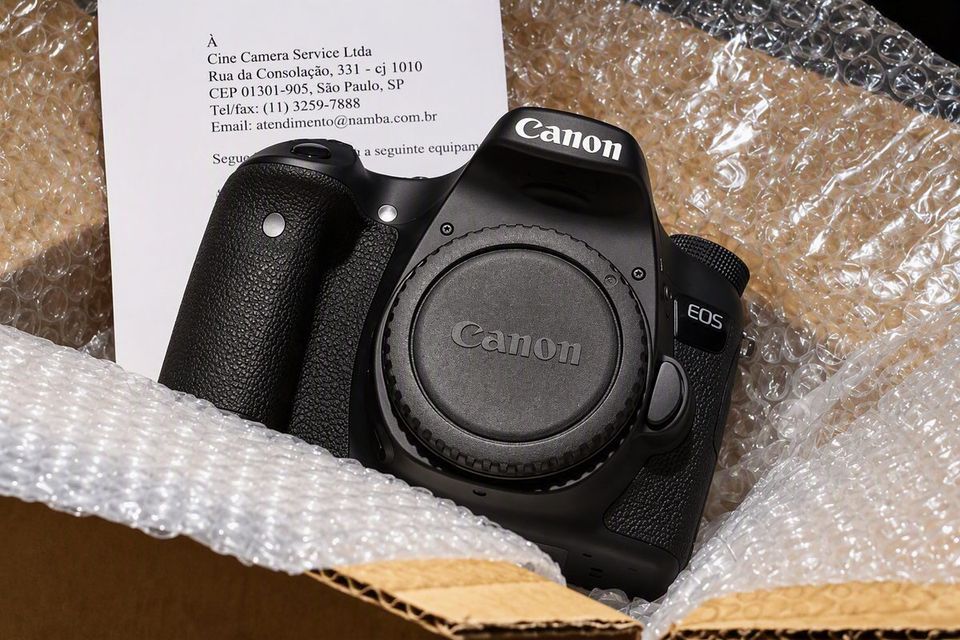 Câmera Canon EOS dentro de uma caixa com plástico-bolha, com a carta de envio impressa ao lado